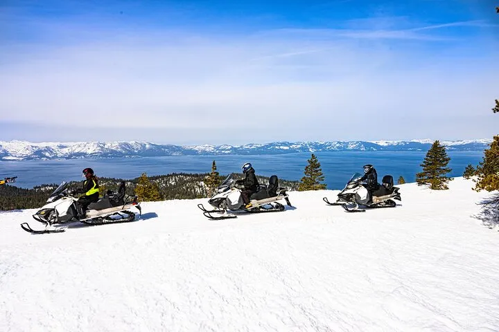 A guided snowmobile group on a snowy ridge above Zephyr Cove on a Lake Tahoe snowmobile tour with the lake below